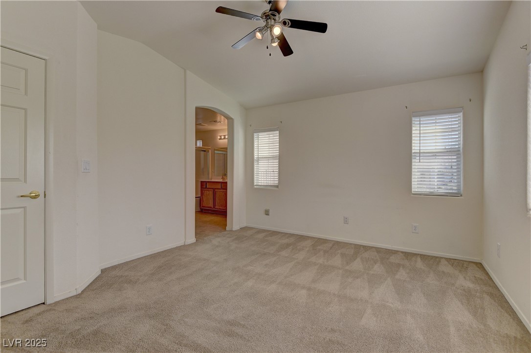10403 Madagascar Palm Street Las Vegas, NV 89141 - Photo 15 of 21 Unfurnished bedroom with multiple windows, light colored carpet, ensuite bathroom, arched walkways, and vaulted ceiling