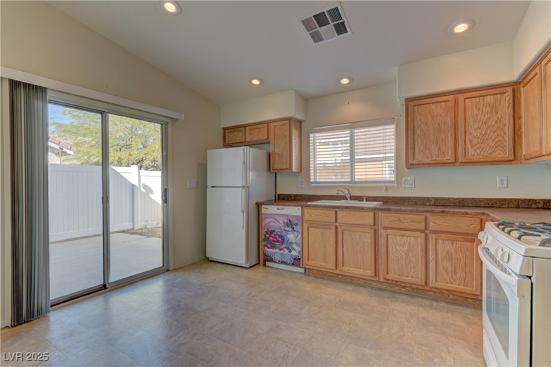 10403 Madagascar Palm Street Las Vegas, NV 89141 - Photo 10 of 21 Kitchen with dark countertops, white appliances, recessed lighting, light brown cabinets, and lofted ceiling