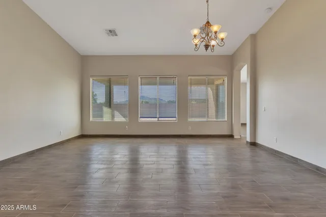 a view of an empty room with chandelier fan and wooden floor