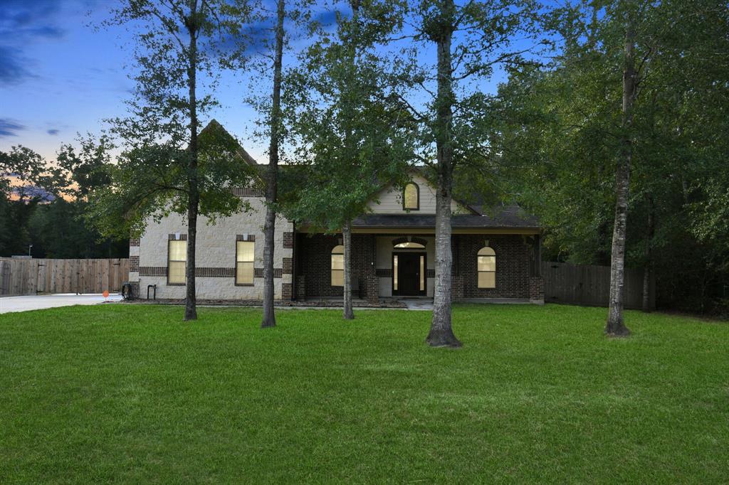 a view of house in front of a big yard with large trees and wooden fence