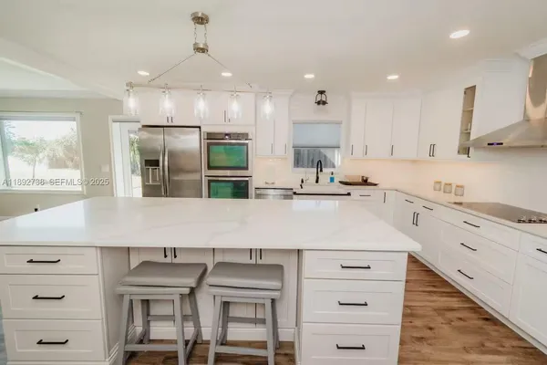 a large white kitchen with granite countertop a stove a sink dishwasher and a refrigerator with wooden floor