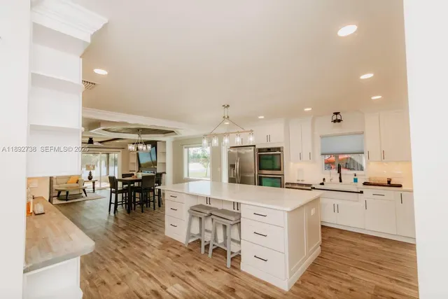 a kitchen with kitchen island a sink a stove a refrigerator and white cabinets with wooden floor
