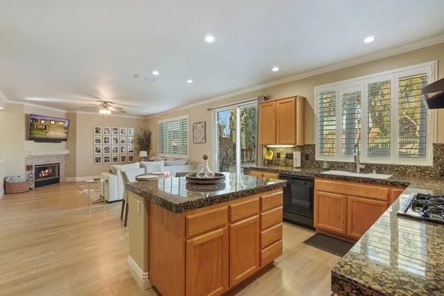 a kitchen with stainless steel appliances granite countertop a stove a sink a refrigerator white cabinets and couches with wooden floor