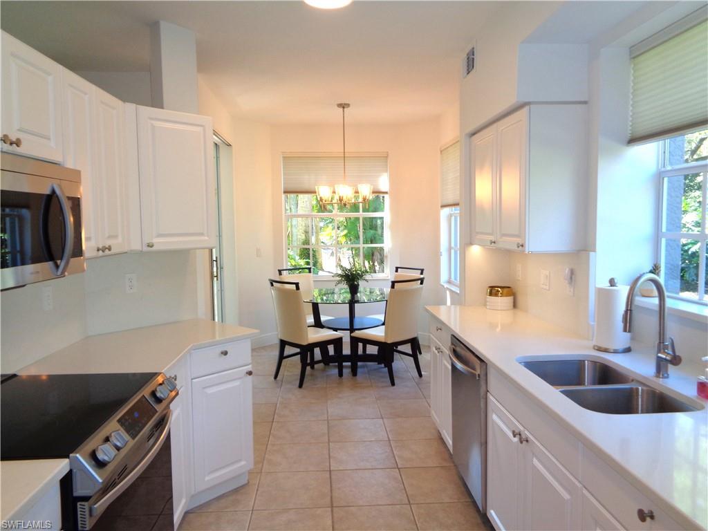 515 Laguna Royale Boulevard, Unit 102 Naples, FL 34119 - Photo 11 of 28 Kitchen with light tile patterned flooring, a sink, a chandelier, white cabinetry, and stainless steel appliances