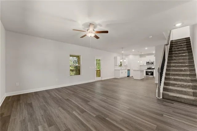 a view of an empty room with wooden floor stairs and a ceiling fan