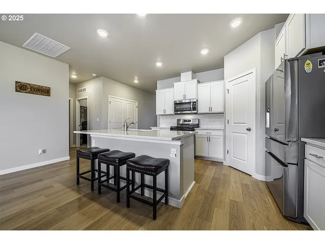 a kitchen with stainless steel appliances kitchen island granite countertop a refrigerator a stove a sink dishwasher and white cabinets with wooden floor