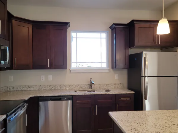 a kitchen with granite countertop a refrigerator a sink and wooden cabinets