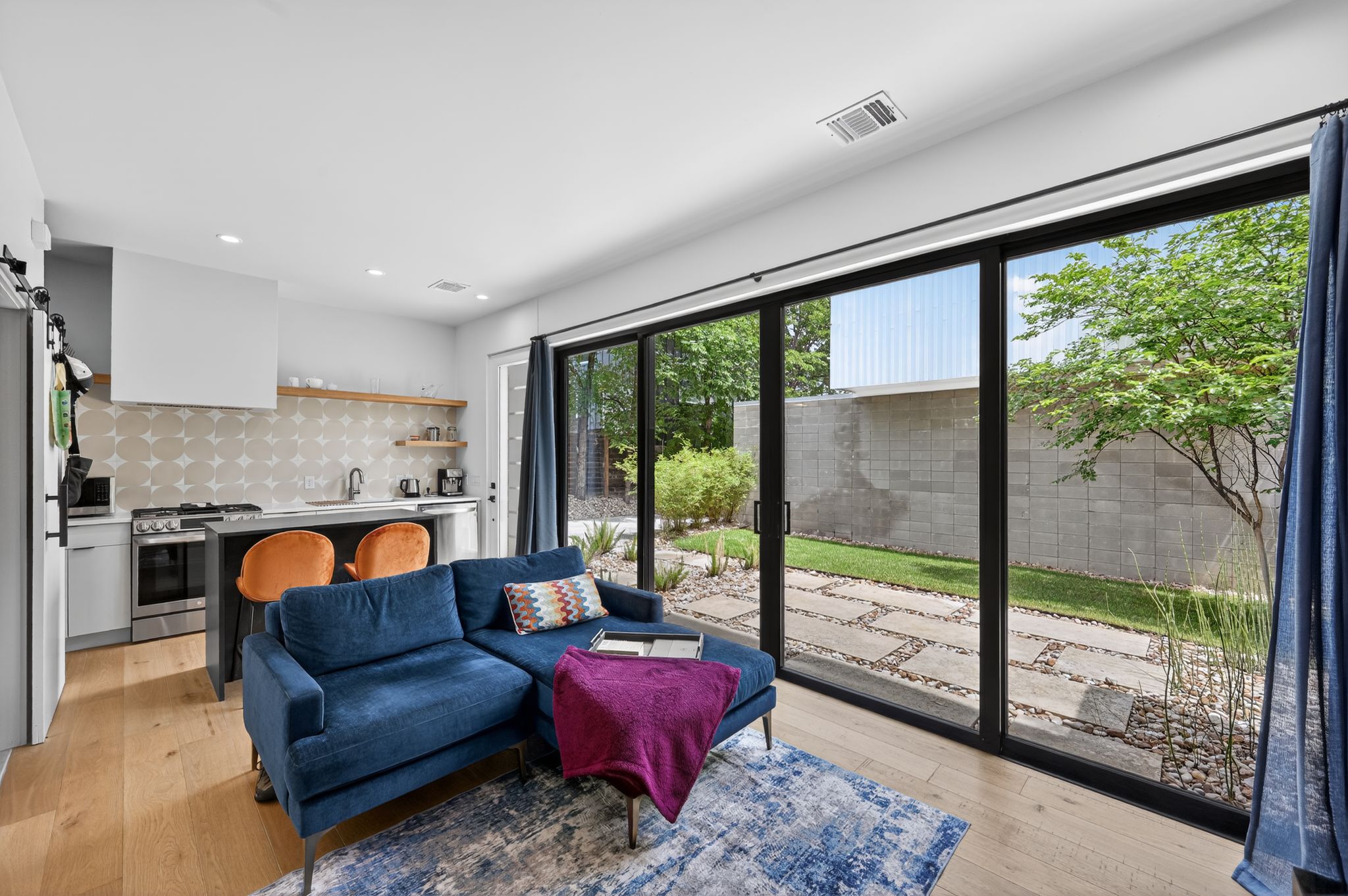 1206 Luna Street, Unit 2 Austin, TX 78721 - Photo 14 of 30 Open concept living area with hardwood flooring, a kitchen featuring a patterned tile backsplash and stainless steel appliances, and a large sliding glass door opening to a private outdoor space