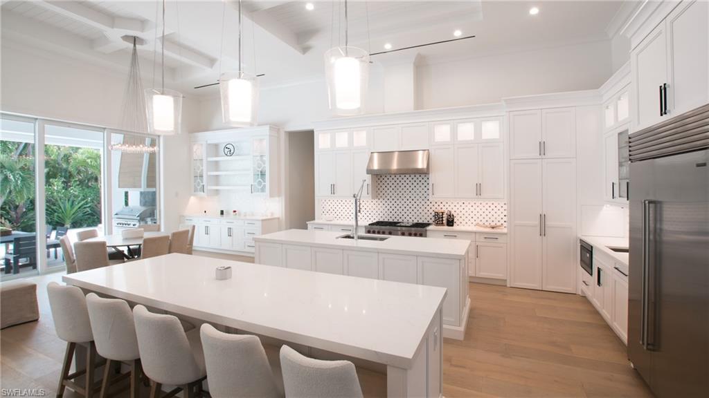 700 Wedge Drive Naples, FL 34103 - Photo 7 of 19 Kitchen featuring stainless steel appliances, wall chimney exhaust hood, beamed ceiling, backsplash, and a kitchen island with sink