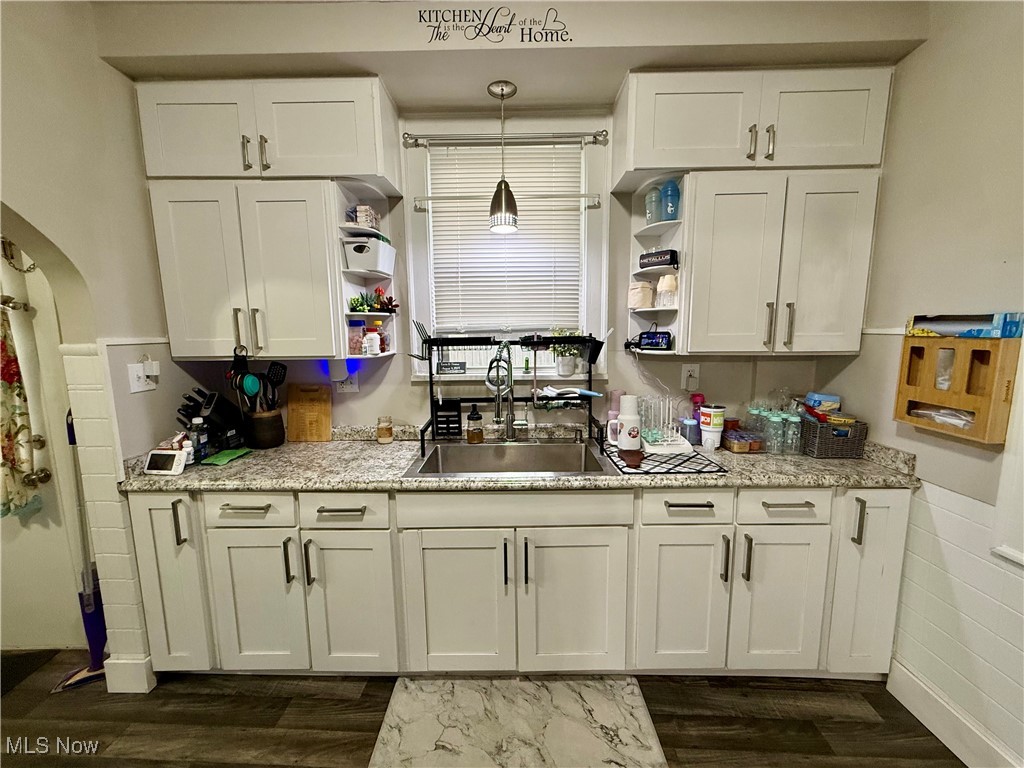 Kitchen with open shelves, white cabinets, dark wood-style floors, pendant lighting, and arched walkways