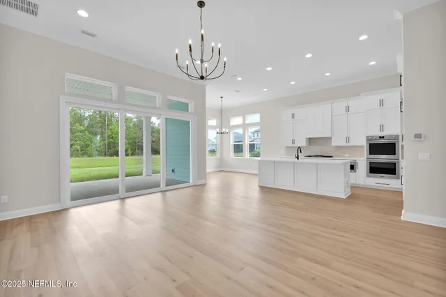 a view of an empty room with wooden floor and a kitchen