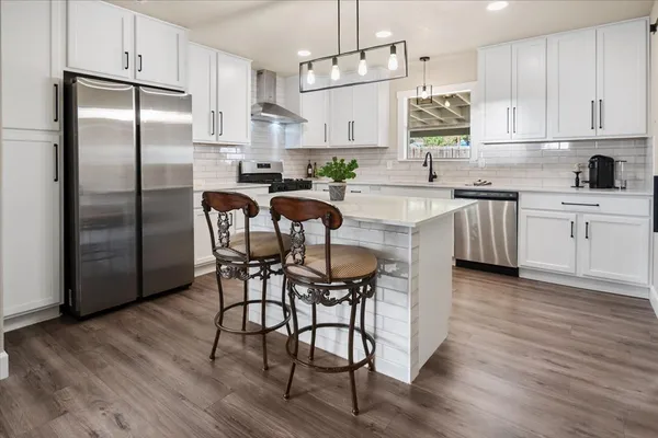 a kitchen with stainless steel appliances granite countertop a white refrigerator a sink a stove a dining table and chairs with wooden floor