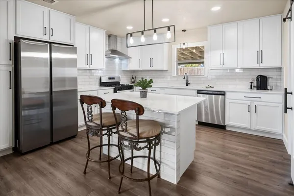 a kitchen with stainless steel appliances granite countertop a dining table chairs refrigerator and microwave