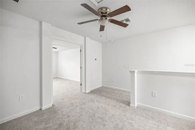 an empty room with a ceiling fan and carpet
