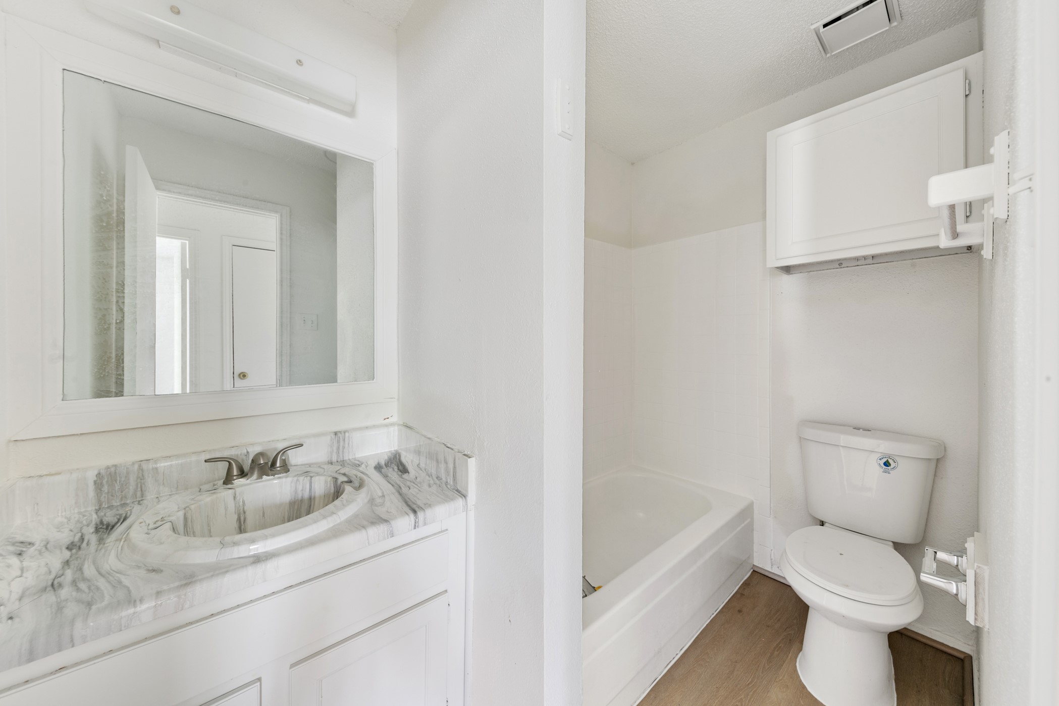 700 Lyle W Avenue, Unit D Cleveland, TX 77327 - Photo 6 of 16 This is a compact bathroom featuring a marble-patterned vanity with a sink, a large mirror, a bathtub, and a toilet. The space has a clean, white aesthetic and includes a wall-mounted cabinet for storage.