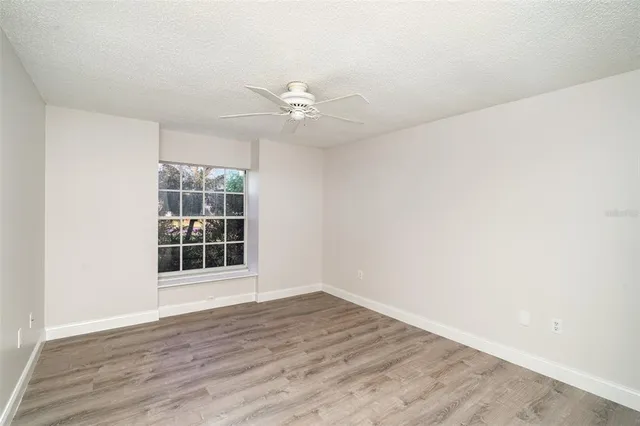 an empty room with wooden floor fan and windows