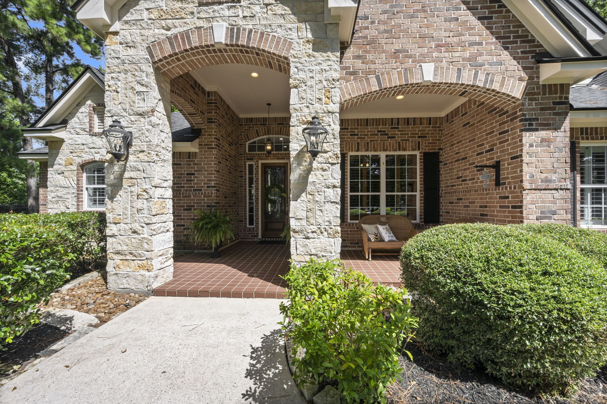 4106 Angling Lane Spring, TX 77386 - Photo 4 of 50 Charming entrance with classic brick and stone archway, enhanced by lush greenery and a cozy seating area on the porch.