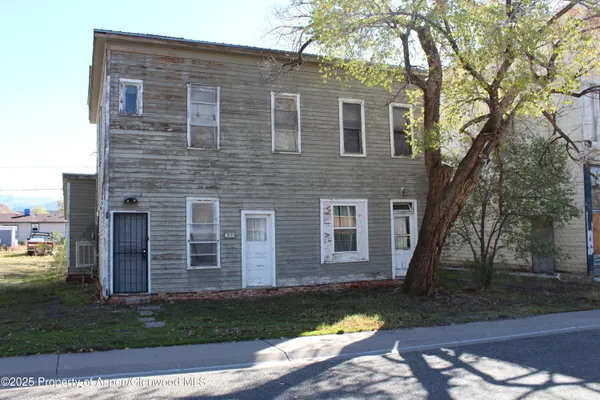 a brick house next to a yard with large trees