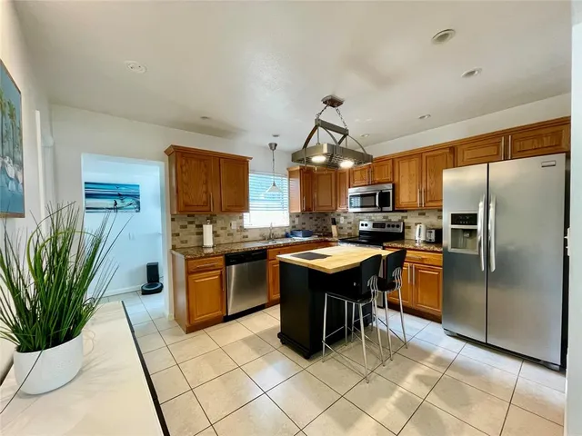 a kitchen with stainless steel appliances granite countertop a refrigerator a sink a stove a dining table and chairs