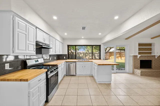 a large kitchen with stainless steel appliances granite countertop a stove top oven a sink dishwasher a dining table and chairs with wooden floor