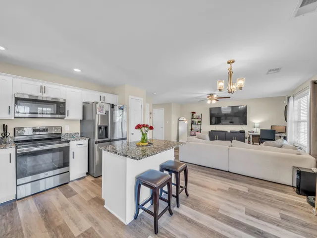 a living room with stainless steel appliances furniture a chandelier and a kitchen view