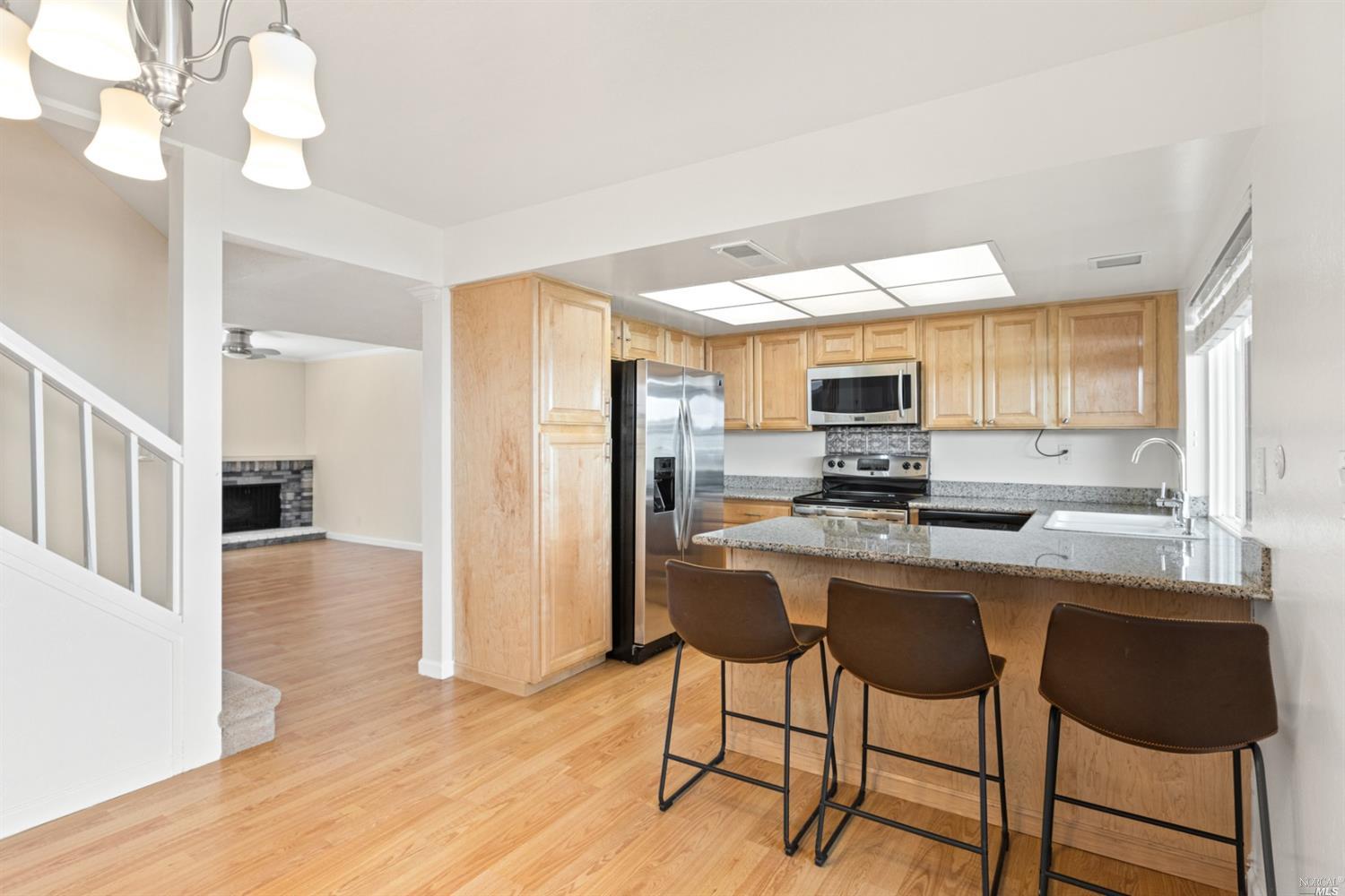 a kitchen with stainless steel appliances granite countertop a stove top oven a refrigerator a sink dishwasher and white cabinets with wooden floor