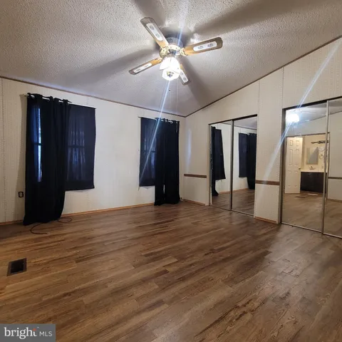 a view of an empty room with wooden floor and a ceiling fan