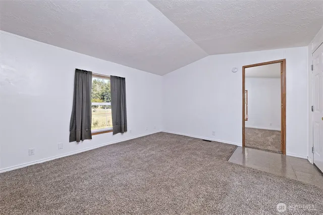 an empty room with windows and view of kitchen