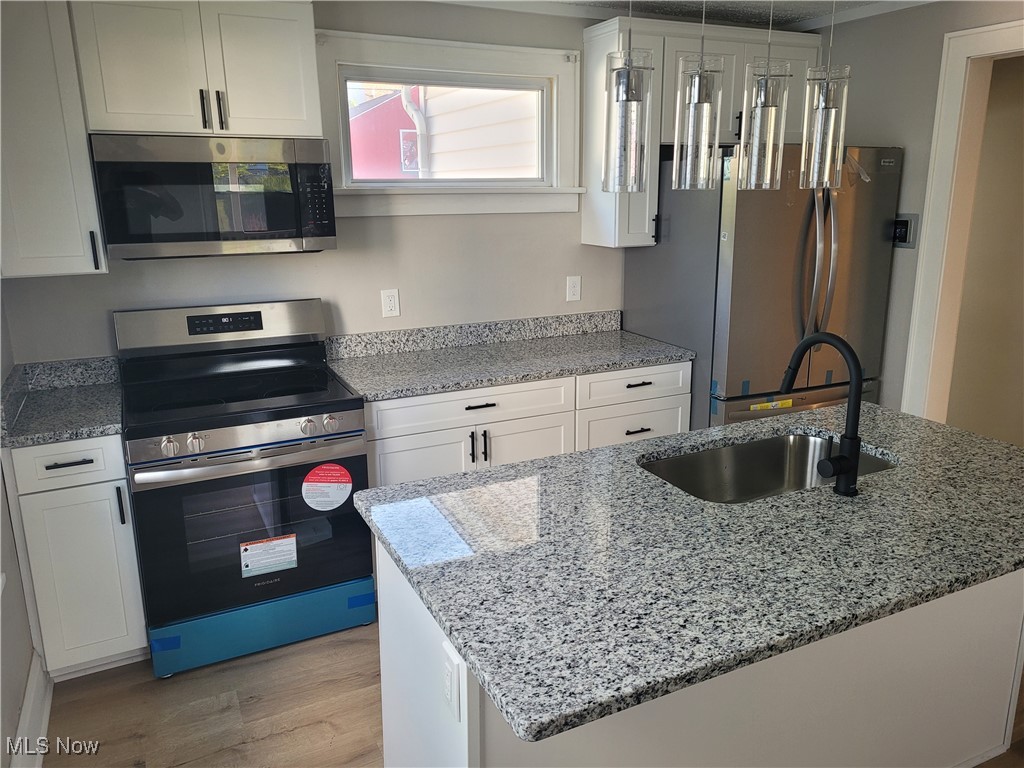 Kitchen featuring white cabinets, stainless steel appliances, light hardwood / wood-style floors, sink, and pendant lighting
