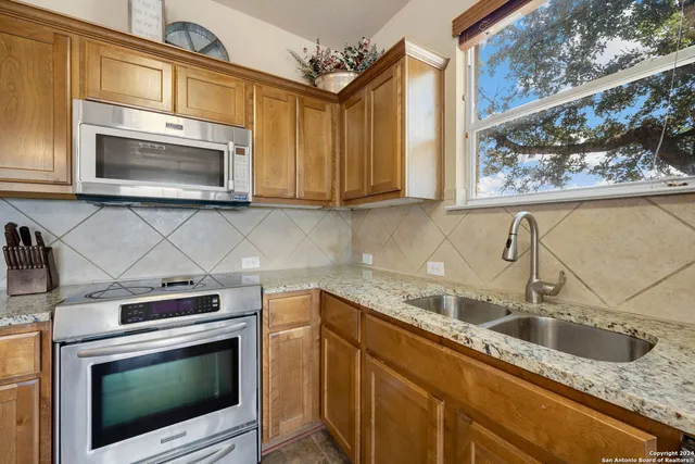 a kitchen with stainless steel appliances granite countertop a sink a stove a microwave and wooden cabinets