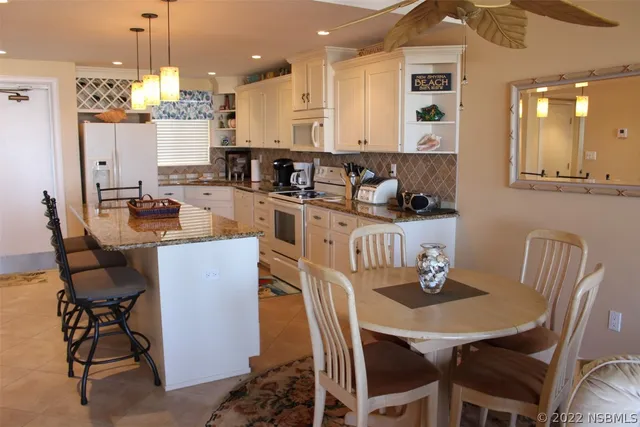 a kitchen with stainless steel appliances kitchen island granite countertop a dining table chairs and a refrigerator