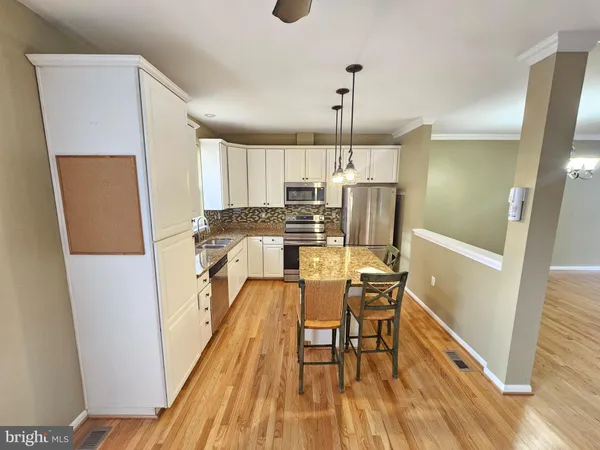 a kitchen with stainless steel appliances a refrigerator a stove a sink dishwasher and white cabinets with wooden floor