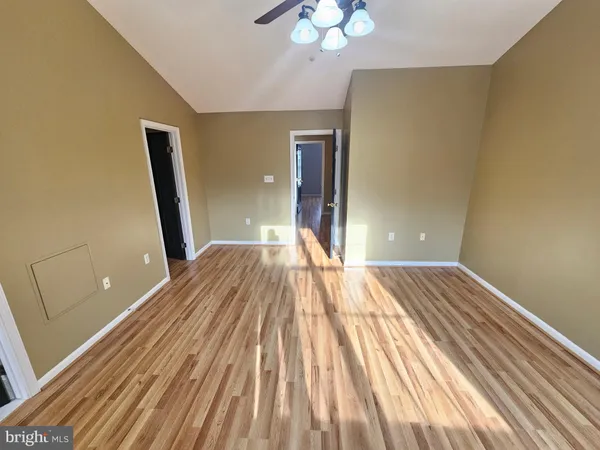 a view of an empty room with wooden floor and a ceiling fan
