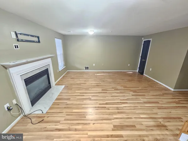 a view of an empty room with wooden floor fireplace and a window