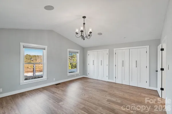 an empty room with wooden floor chandelier and windows