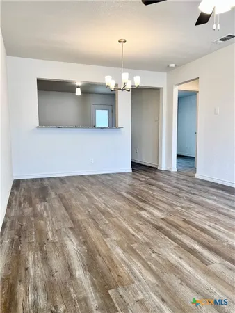 an empty room with kitchen view and wooden floor