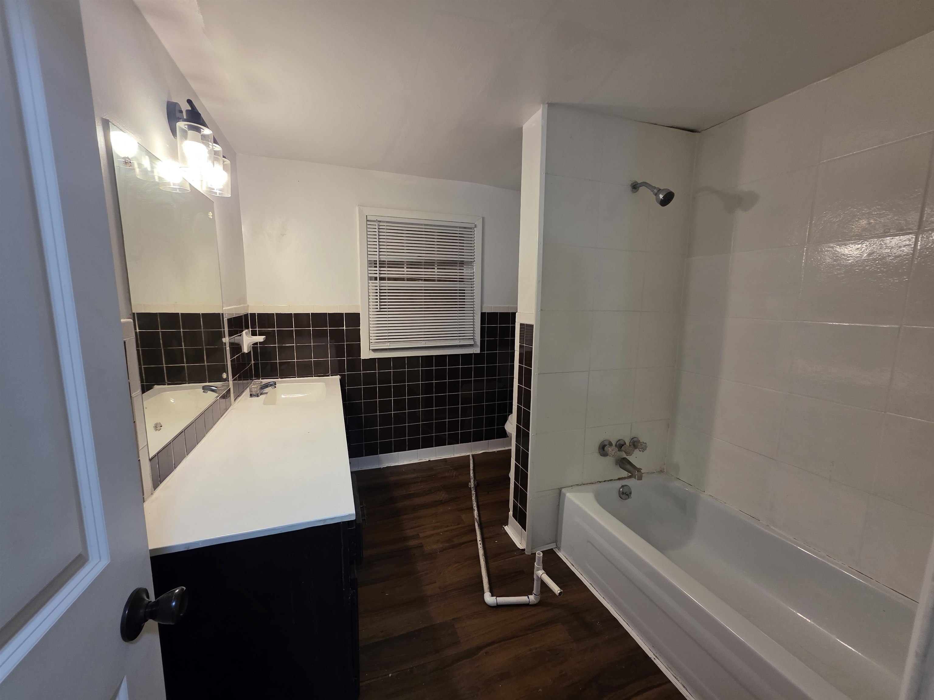 3764 Cazassa Road Memphis, TN 38116 - Photo 15 of 16 Bathroom featuring a white bathtub, black and white tiled walls, a single vanity with a white countertop, a wall-mounted mirror, and wood-finish flooring