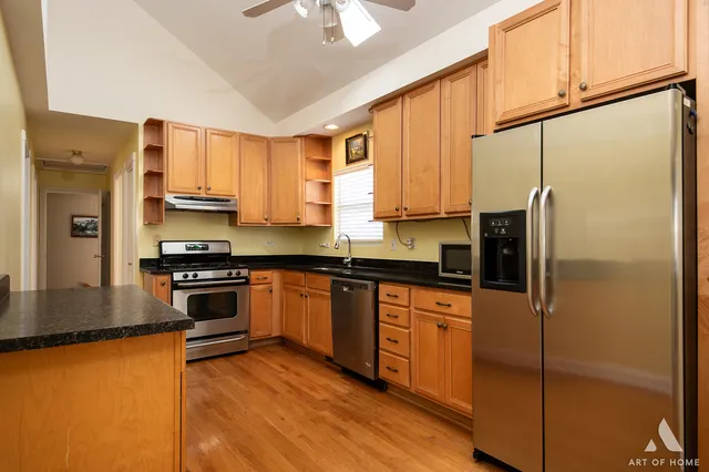 a kitchen with stainless steel appliances granite countertop a refrigerator a stove and a sink with wooden floor