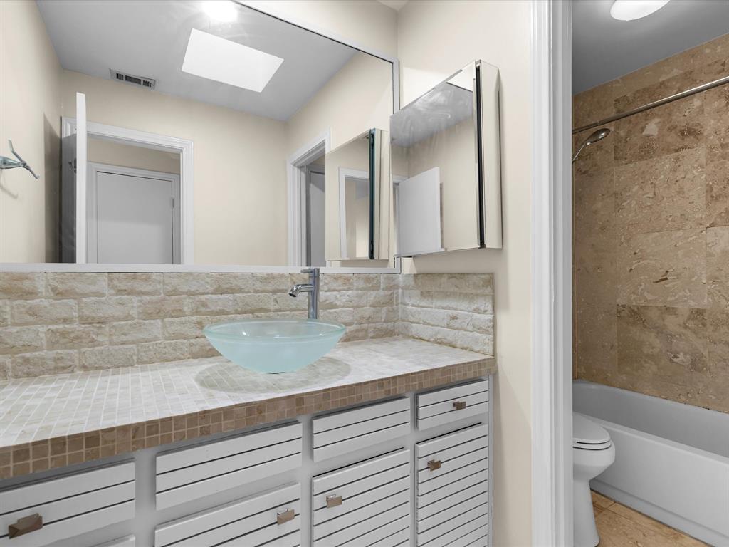 4110 Travis Street, Unit E Dallas, TX 75204 - Photo 20 of 23 a bathroom with a granite countertop sink a toilet a mirror and shower