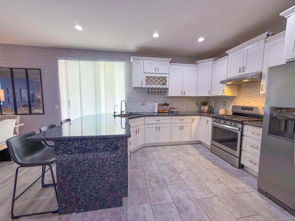 3237 Warley Road Hemet, CA 92545 - Photo 14 of 43 a large kitchen with granite countertop a stove a sink a refrigerator and white cabinets with wooden floor