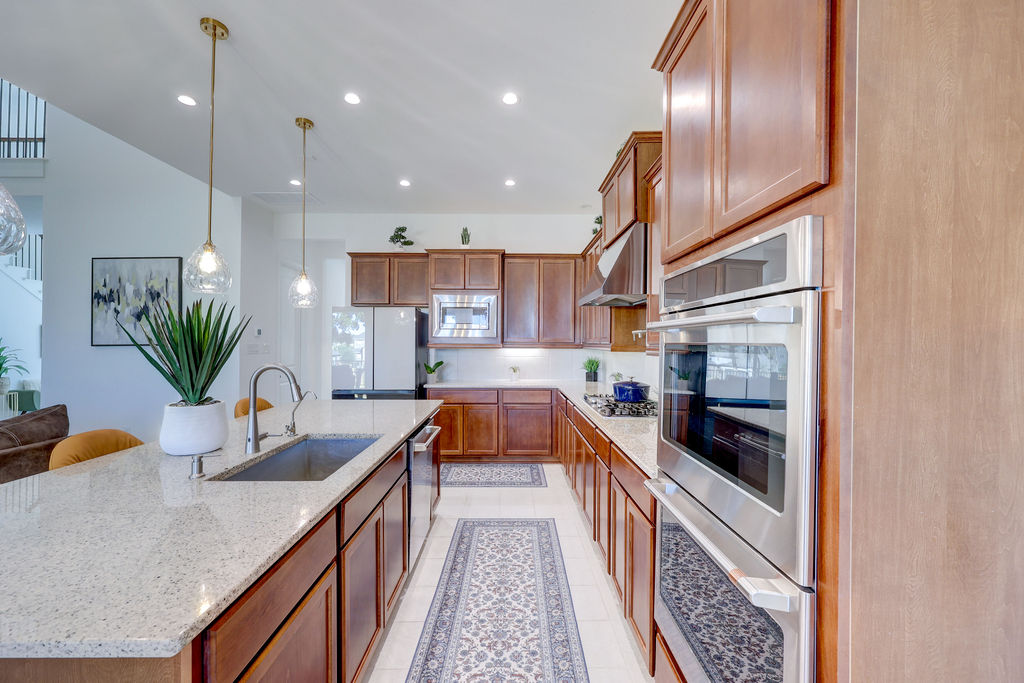 351 Pigeon River Road Kyle, TX 78640 - Photo 14 of 40 Kitchen with appliances with stainless steel finishes, recessed lighting, light stone counters, decorative light fixtures, and brown cabinetry