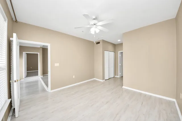 an empty room with wooden floor chandelier fan and windows