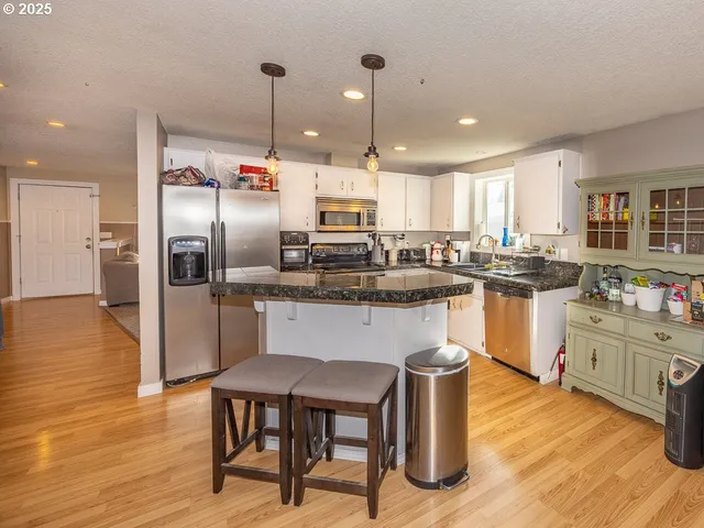 a kitchen with stainless steel appliances granite countertop a stove a sink a refrigerator and white cabinets with wooden floor