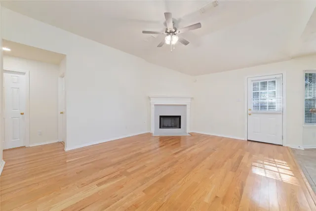 a view of an empty room with window and chandelier fan