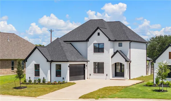 a view of a white house with yard plants and large tree