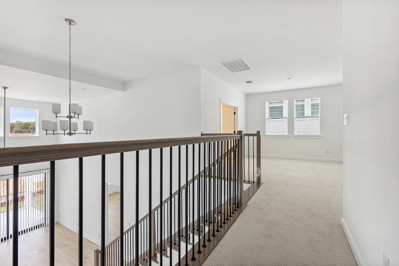 1909 Varese Path Leander, TX 78641 - Photo 25 of 40 A striking contemporary chandelier illuminates the open-concept living area and staircase with dark wood railings.