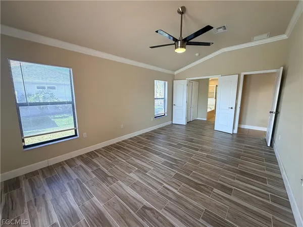 a view of an empty room with wooden floor and a ceiling fan
