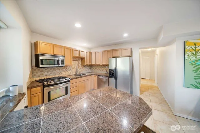 a kitchen with stainless steel appliances granite countertop a stove a refrigerator a sink a oven with wooden cabinets and floor