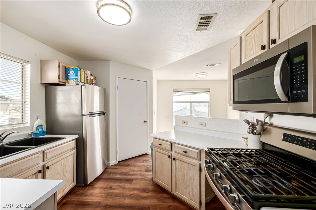 698 South Racetrack Road, Unit 124 Henderson, NV 89015 - Photo 11 of 29 Kitchen with light wood finish cabinets, stainless steel appliances, light countertops, dark wood finished floors, and a peninsula
