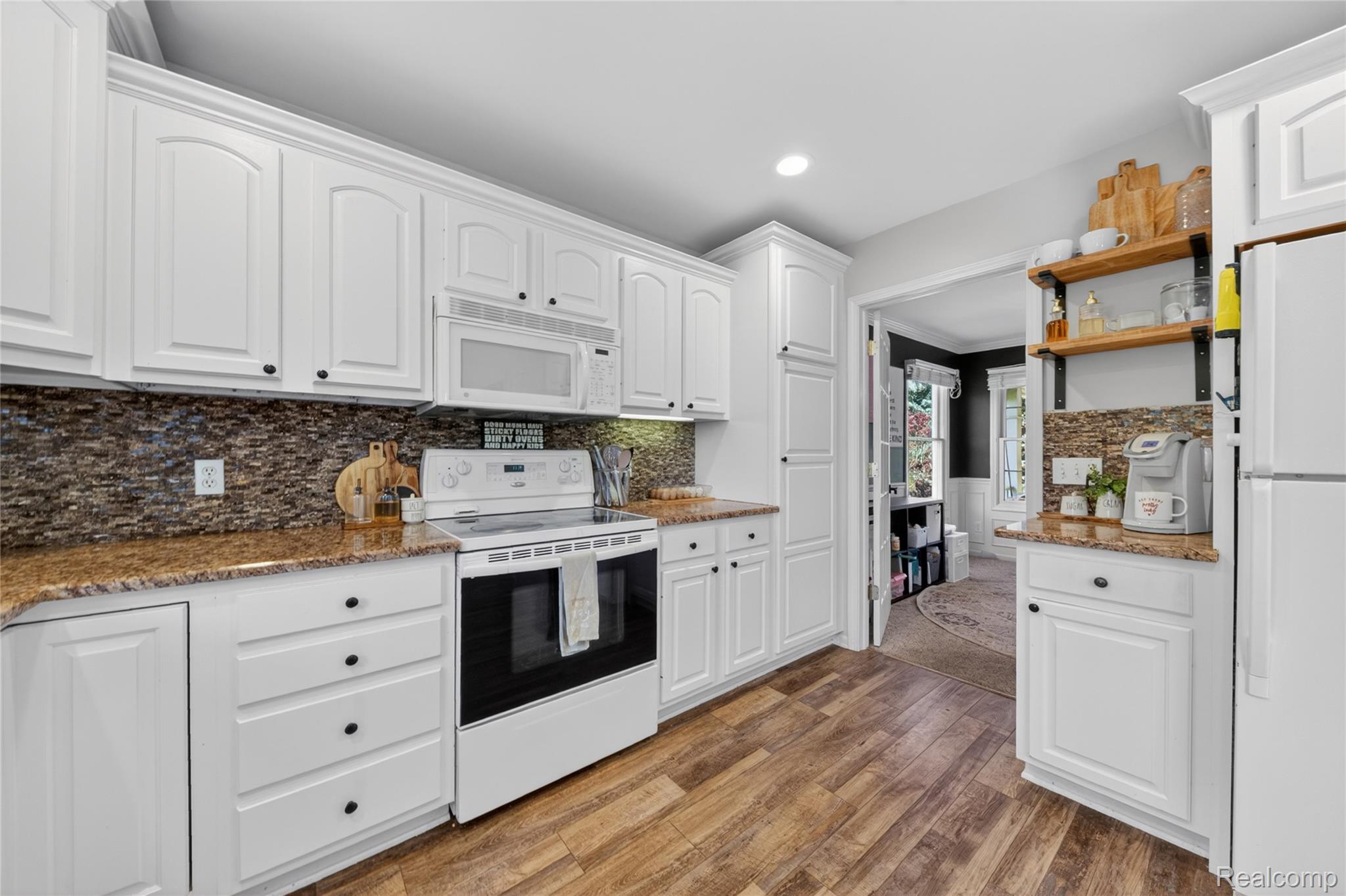 9191 Judd Road Fowlerville, MI 48836 - Photo 11 of 74 White cabinetry with dark hardware, stone countertops, mosaic tile backsplash, wood-finish flooring, and integrated white appliances